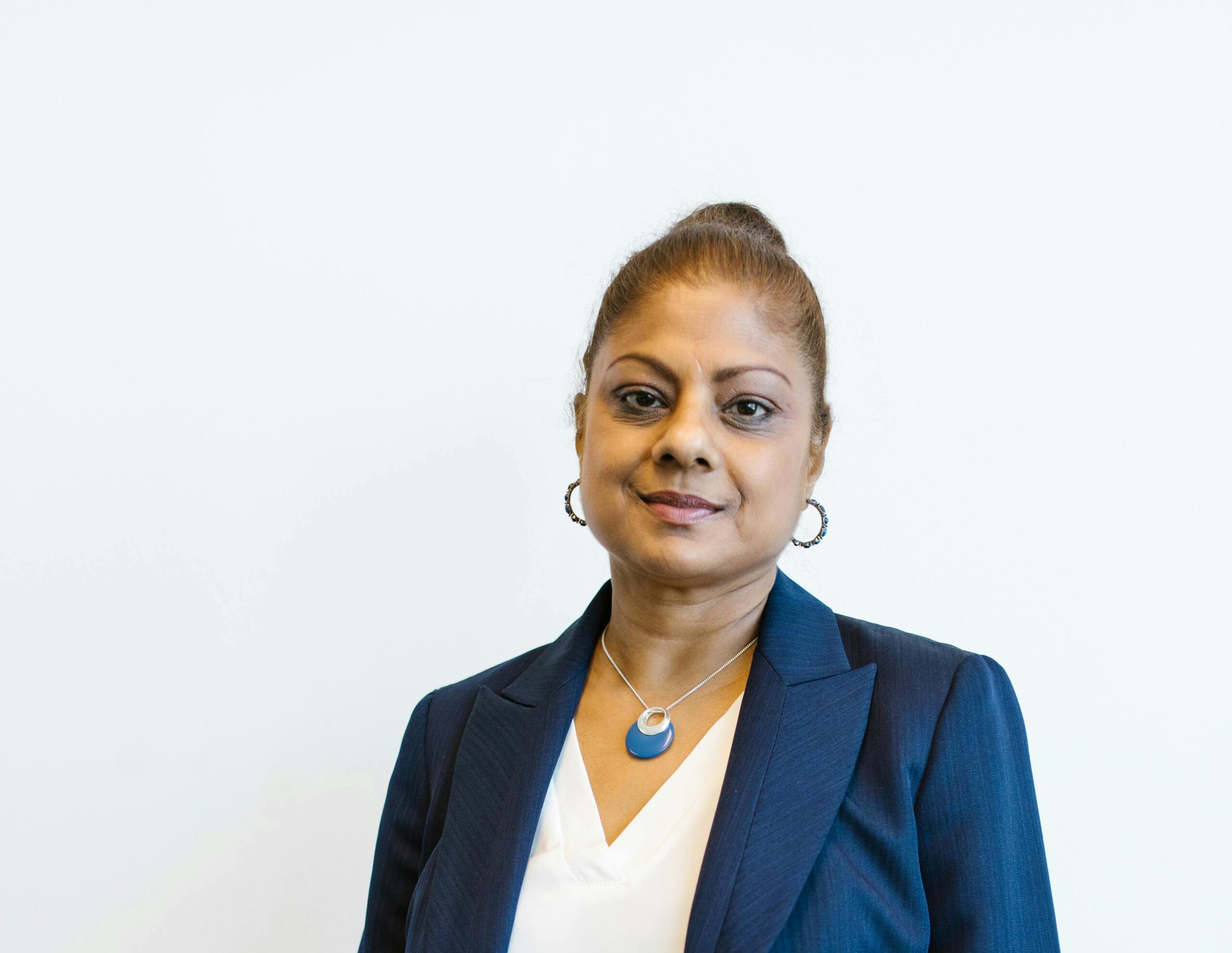 Professional headshot of a woman wearing a navy blue suit and white blouse, standing against a light gray background.
